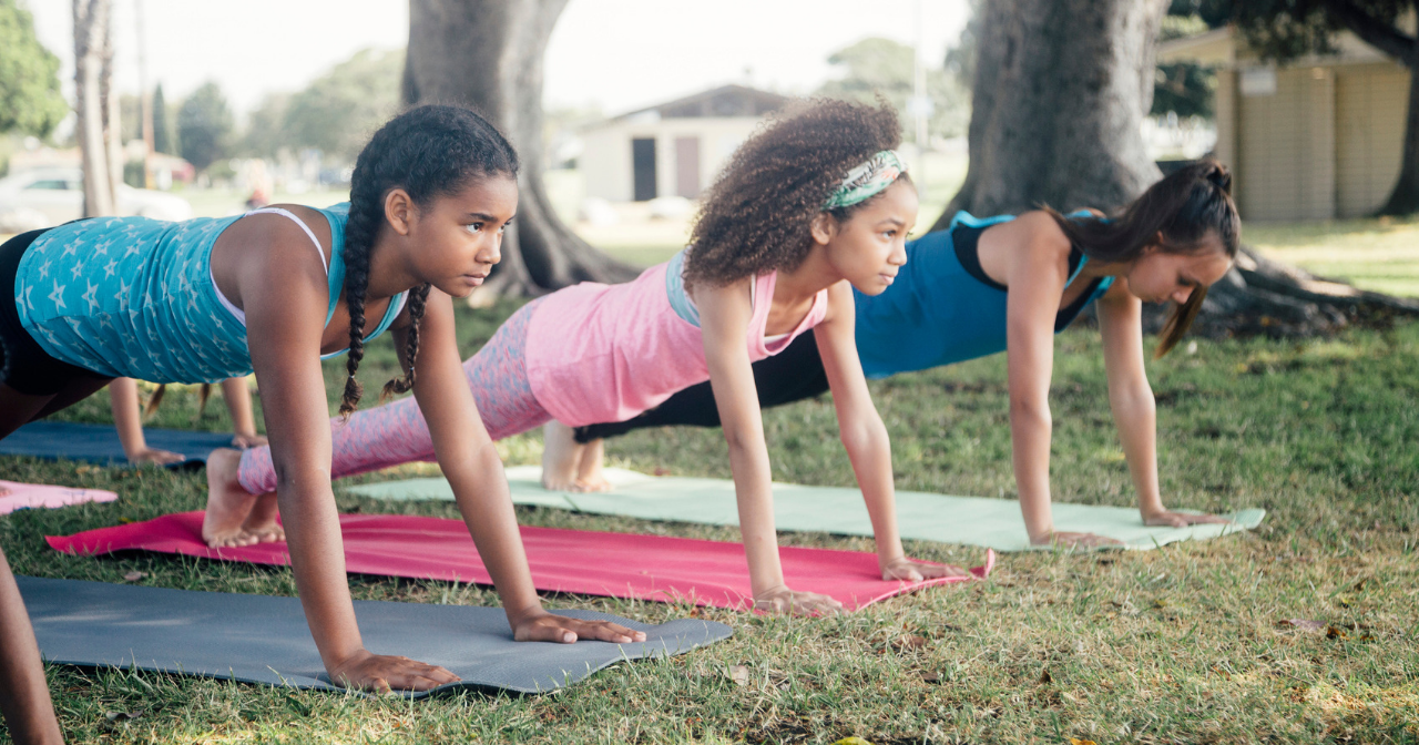 Three young girls do yoga outdoors