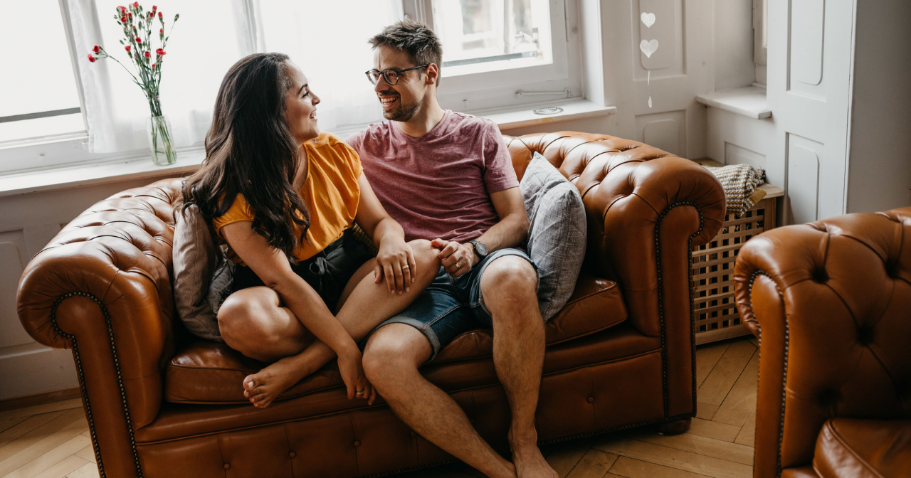 A heterosexual couple sits on a sofa and chats. 