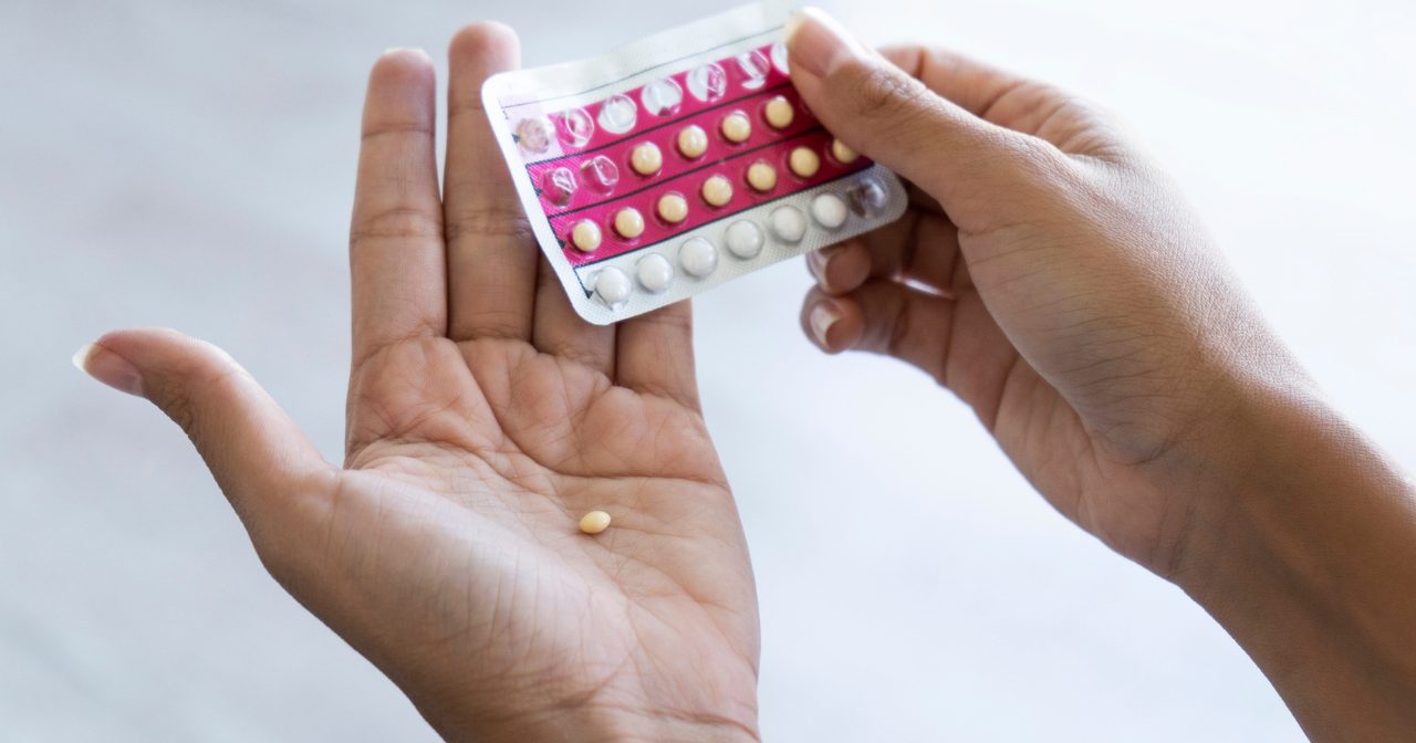 A photo of a pair of hands, one holding a packet of birth control pills and the other with a single pill resting in the palm. 