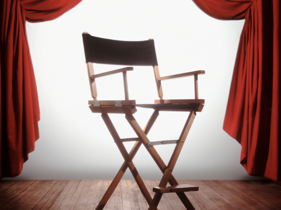 A classic director's chair sits backlit between two red velvet curtains. 