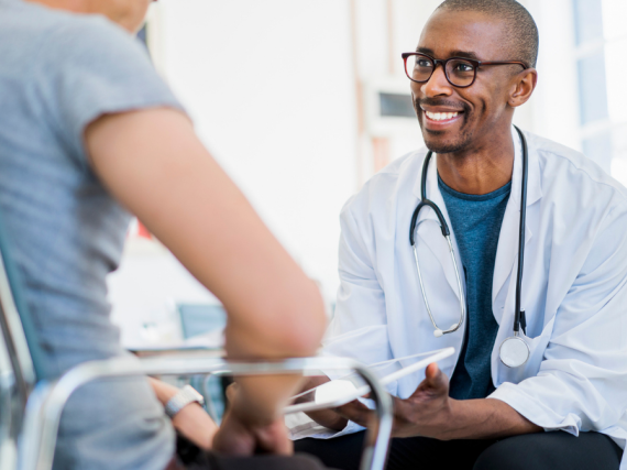 A male doctor speaks to a male patient with a smile on his face. 