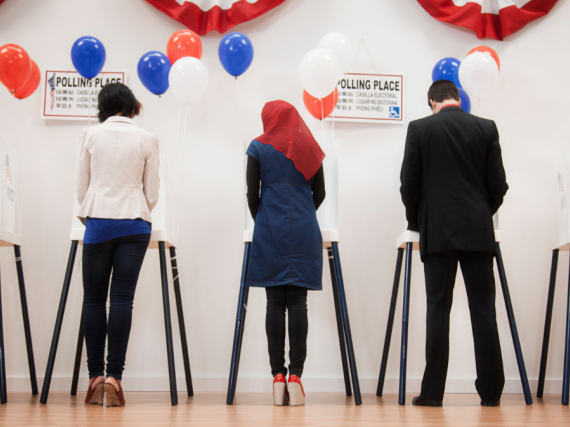 Two men and three women stand at voting booths and cast their ballots. 