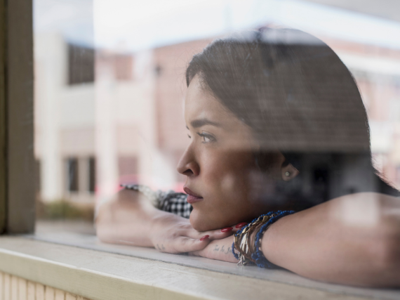 A woman looks out a window contemplatively. 