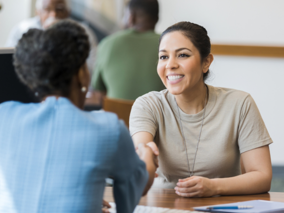 A servicewoman shakes hands with another woman from across a desk. 