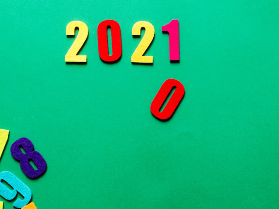 Refrigerator magnets in the shape of numbers sit on a green background. 2021 is spelled out with a zero falling down under where the 1 sits. 