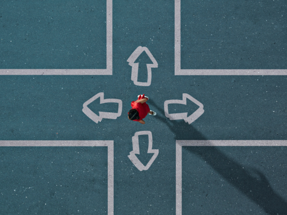 An overhead photo of a woman dressed in red stands in the middle of a painted intersection deciding which way to go. 