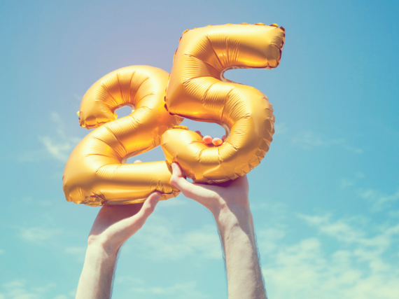 Hands hold golden balloons with the numbers 2 and 5 up to the sky. 