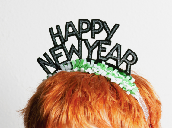 A photo of a the top of a person's head. They have red hair and are wearing a novelty headband that reads happy new year.