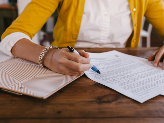 A photo of a woman signing some papers on a desk. 