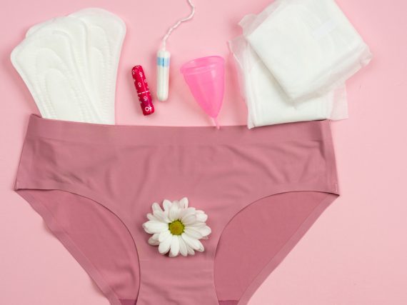 A pair of underwear lay spread out against a pink background with a number of period products scattered around. 