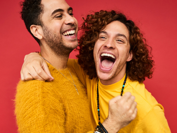 Two men in a relationship laugh and hug for a photo. 