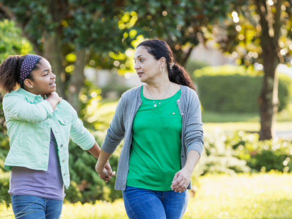 Mom and daughter walk outside hand in hand and talk. 