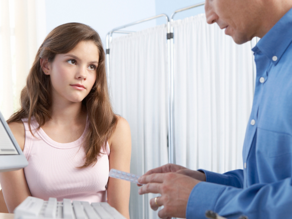 A male provider talks to a young teen about birth control while holding a packet of birth control pills. 