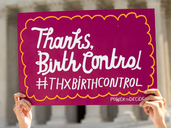 Hands holding a sign that reads, "Thanks, Birth Control #ThxBirthControl" outside the Supreme Court. 